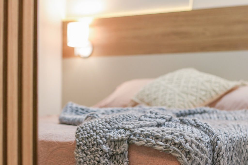 Cama com arandela acesa, manta de tricô e camadas de textura macia